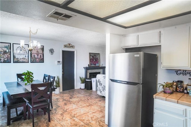 kitchen featuring stainless steel refrigerator, white cabinetry, tile counters, hanging light fixtures, and a chandelier