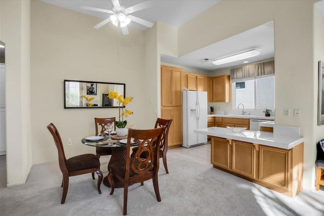 kitchen featuring kitchen peninsula, white appliances, light colored carpet, ceiling fan, and sink