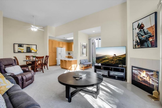 living room with ceiling fan, lofted ceiling, light carpet, and a tile fireplace