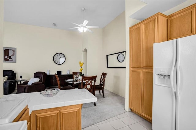 kitchen with kitchen peninsula, light carpet, ceiling fan, tile countertops, and white fridge with ice dispenser