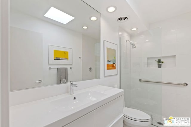 bathroom with a tile shower, a skylight, vanity, and toilet