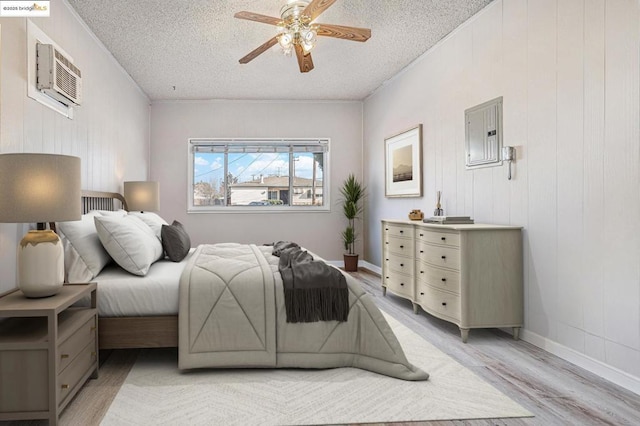 bedroom with ceiling fan, light wood-type flooring, a textured ceiling, and a wall unit AC