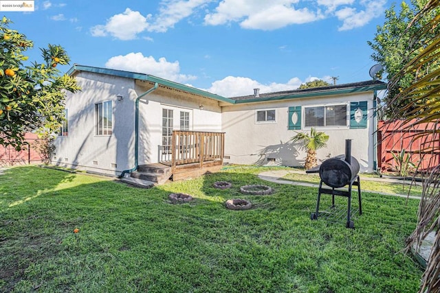 back of property featuring a fire pit, a deck, and a yard