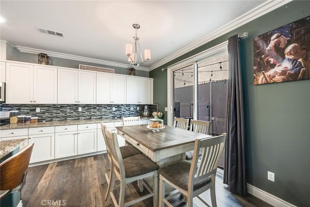 kitchen with light stone countertops, dark wood-type flooring, hanging light fixtures, crown molding, and white cabinets