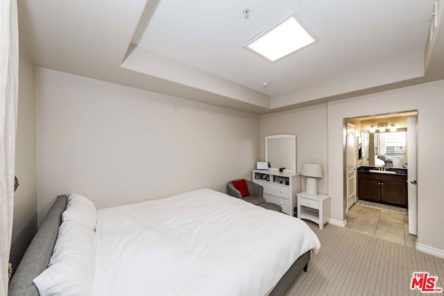 bedroom with a raised ceiling, ensuite bathroom, sink, and light tile patterned floors