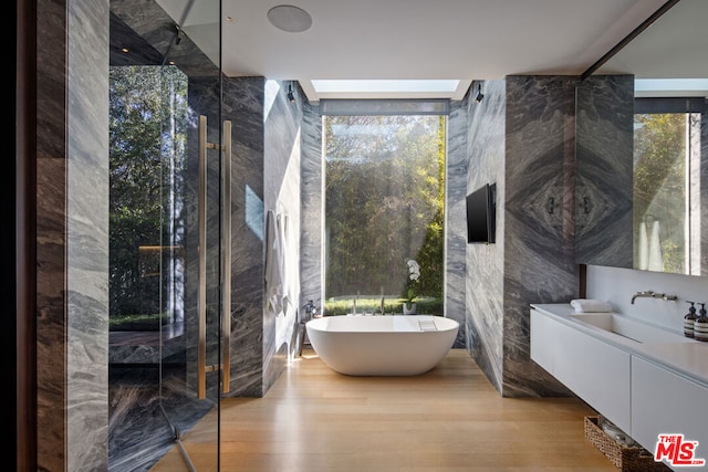 bathroom featuring a bathing tub, floor to ceiling windows, hardwood / wood-style floors, vanity, and tile walls