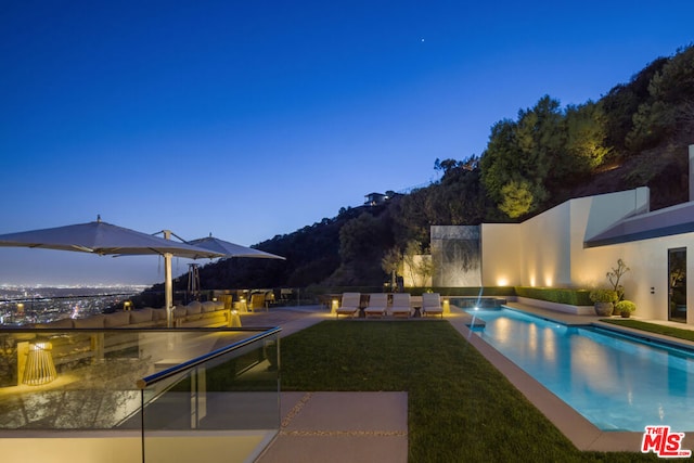 pool at dusk featuring a lawn and a patio area