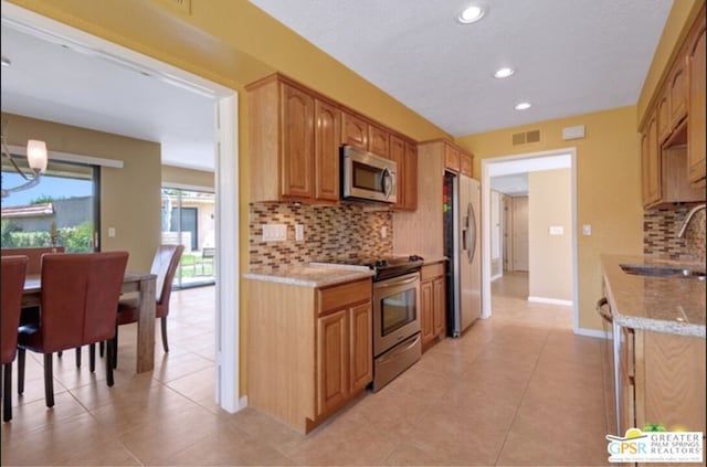 kitchen with decorative backsplash, light stone counters, stainless steel appliances, sink, and a notable chandelier