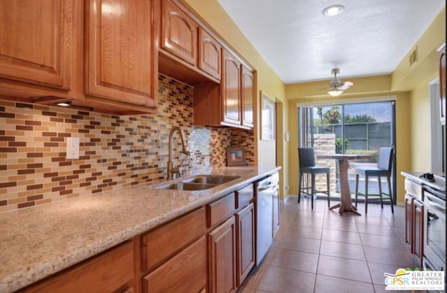 kitchen with ceiling fan, sink, dishwashing machine, light stone counters, and decorative backsplash