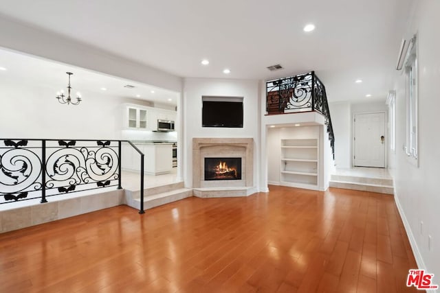 unfurnished living room featuring light hardwood / wood-style floors, a notable chandelier, built in features, and a premium fireplace