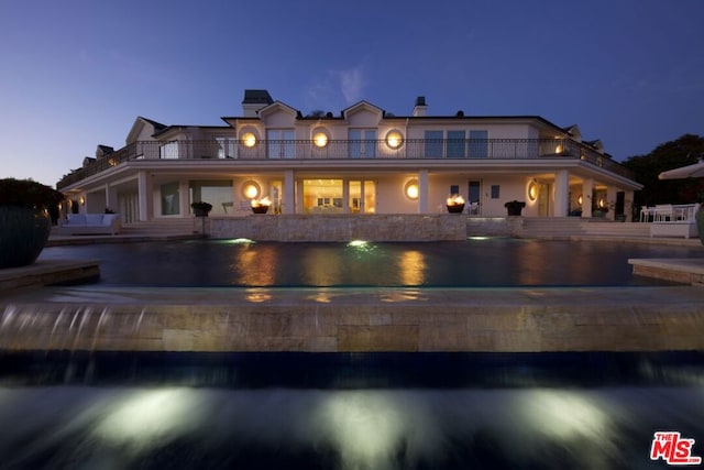 back house at dusk with a balcony and a water view