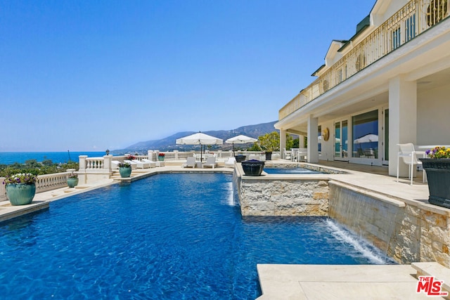 view of pool featuring a patio area, pool water feature, a water and mountain view, and a hot tub