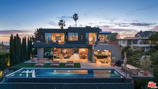 back house at dusk with an outdoor living space, a balcony, a patio, and a pool with hot tub