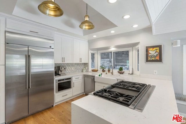 kitchen with appliances with stainless steel finishes, light wood-type flooring, a tray ceiling, white cabinetry, and hanging light fixtures