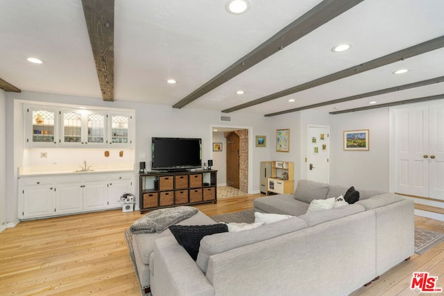 living room featuring beam ceiling, light hardwood / wood-style flooring, and indoor wet bar