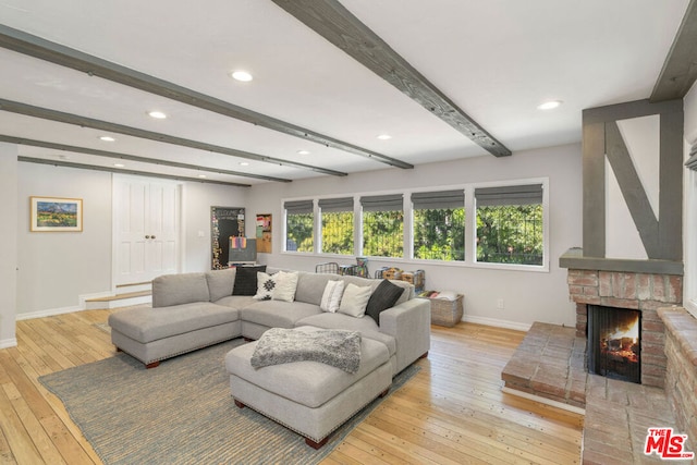 living room featuring a brick fireplace, beam ceiling, a wealth of natural light, and light hardwood / wood-style flooring