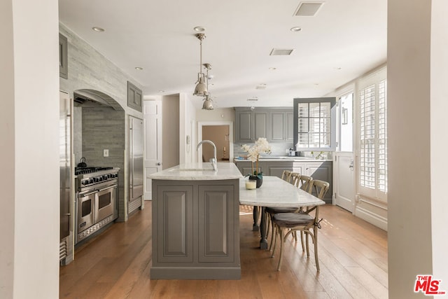 kitchen featuring gray cabinetry, wood-type flooring, high quality appliances, hanging light fixtures, and an island with sink