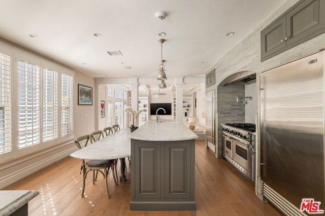 kitchen with high quality appliances, a kitchen island with sink, decorative light fixtures, dark hardwood / wood-style flooring, and light stone counters