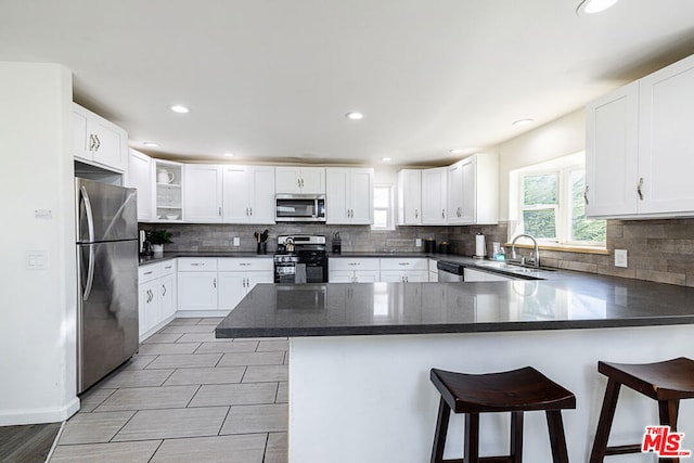 kitchen featuring white cabinets, a kitchen bar, kitchen peninsula, and stainless steel appliances