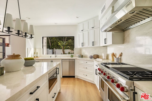 kitchen with wall chimney exhaust hood, light hardwood / wood-style flooring, decorative light fixtures, white cabinets, and appliances with stainless steel finishes