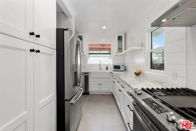 kitchen with light stone counters, ventilation hood, stainless steel appliances, light tile patterned floors, and white cabinets