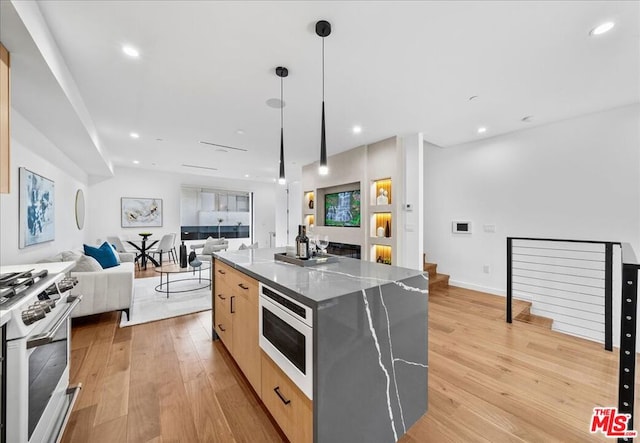 kitchen with light brown cabinets, hanging light fixtures, built in microwave, a kitchen island, and white range with gas cooktop