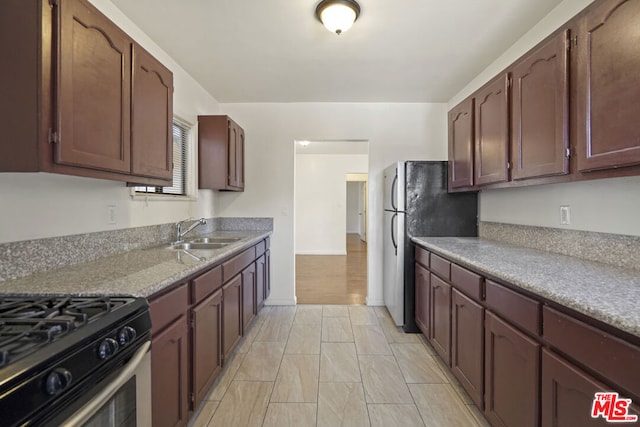 kitchen featuring light stone countertops, range with gas cooktop, stainless steel refrigerator, and sink