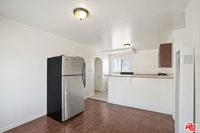 kitchen featuring stainless steel refrigerator, kitchen peninsula, and dark wood-type flooring