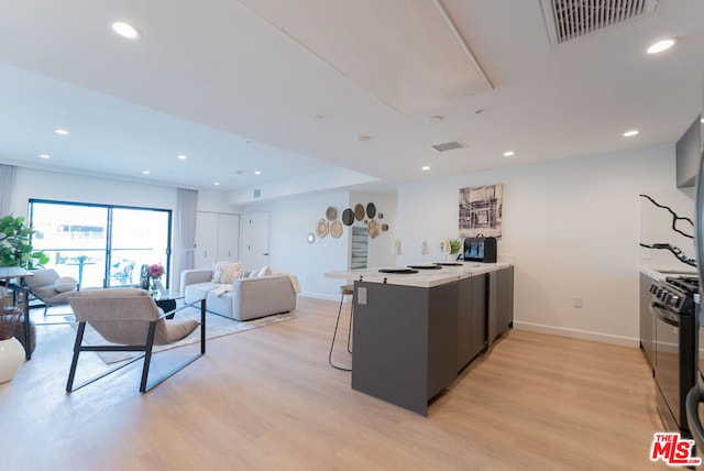 kitchen with black range, light hardwood / wood-style floors, a kitchen bar, and kitchen peninsula