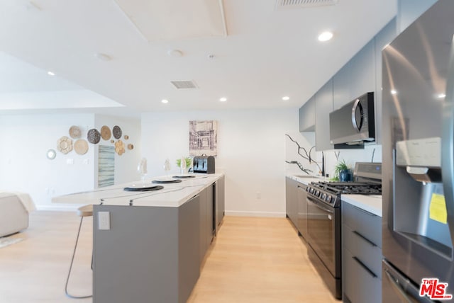 kitchen featuring gray cabinetry, a kitchen breakfast bar, light wood-type flooring, and appliances with stainless steel finishes