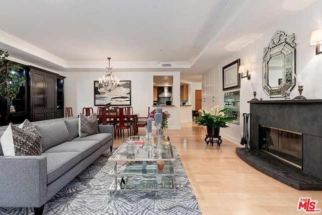 living room featuring a high end fireplace, hardwood / wood-style flooring, a raised ceiling, and a chandelier