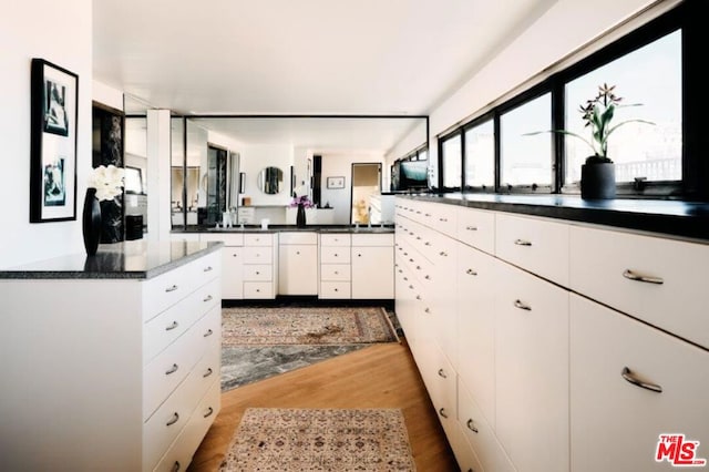 kitchen with dark stone countertops, white cabinetry, and hardwood / wood-style flooring