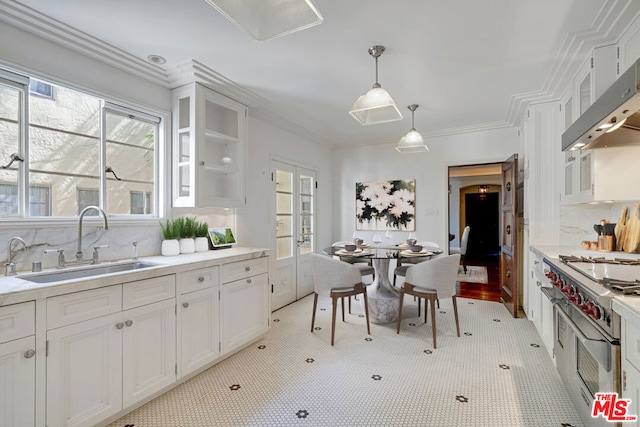 kitchen featuring pendant lighting, exhaust hood, white cabinets, sink, and high end stainless steel range