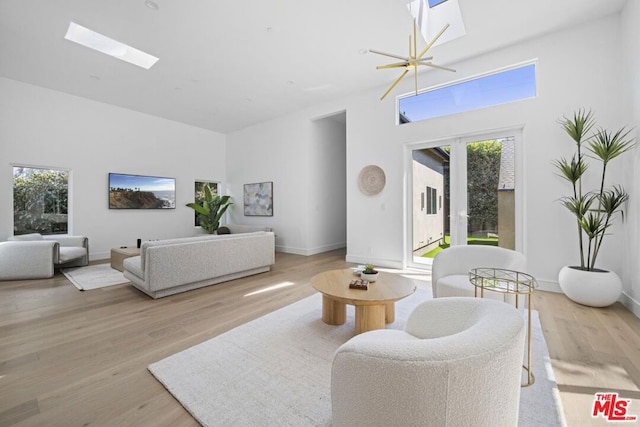 living room with an inviting chandelier, a skylight, light wood-type flooring, and french doors