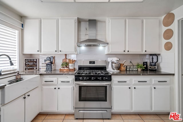 kitchen with a wealth of natural light, wall chimney range hood, stainless steel gas range oven, white cabinets, and light tile patterned floors