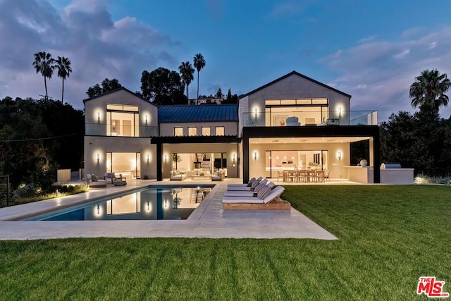 back house at dusk featuring an outdoor hangout area, a balcony, a bar, a patio area, and a yard