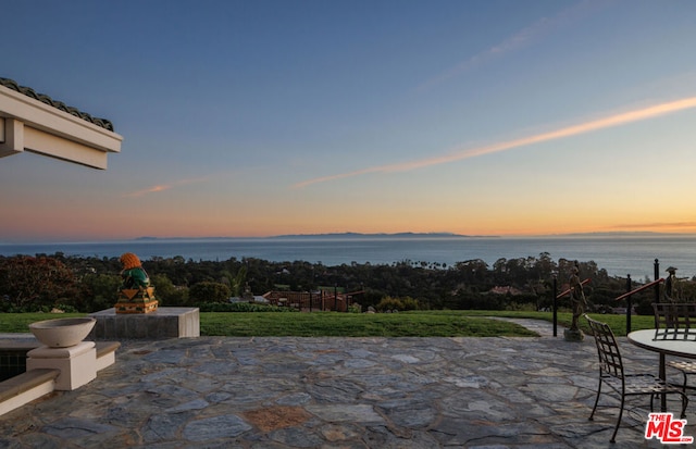 patio terrace at dusk with a water view and an outdoor fireplace