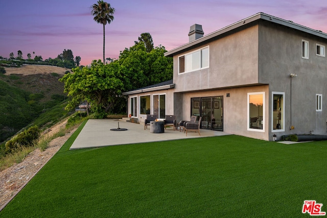 back house at dusk featuring a lawn, an outdoor living space, and a patio