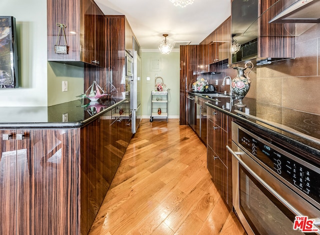 kitchen with appliances with stainless steel finishes, tasteful backsplash, ornamental molding, sink, and light hardwood / wood-style flooring