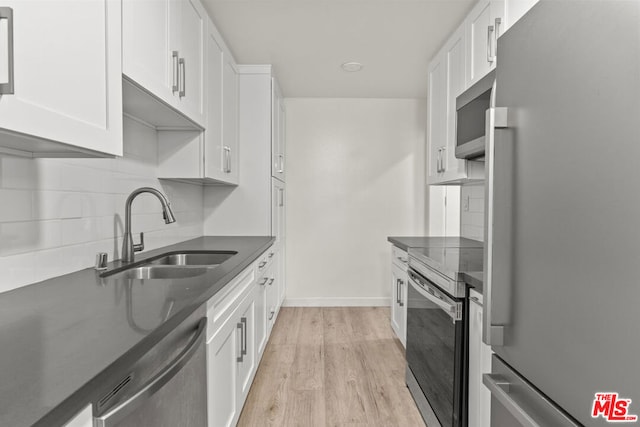 kitchen with appliances with stainless steel finishes, light wood-type flooring, backsplash, sink, and white cabinetry