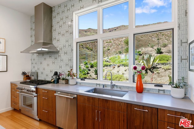 kitchen with appliances with stainless steel finishes, light wood-type flooring, backsplash, wall chimney exhaust hood, and sink