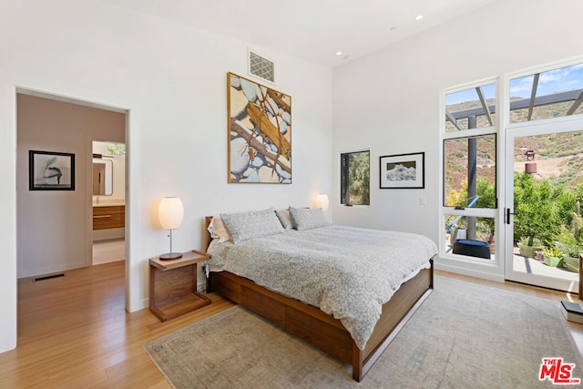 bedroom with access to outside, ensuite bath, light hardwood / wood-style flooring, and a towering ceiling