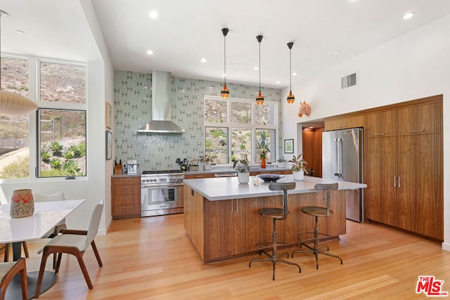 kitchen with a center island, wall chimney range hood, light hardwood / wood-style flooring, pendant lighting, and high quality appliances