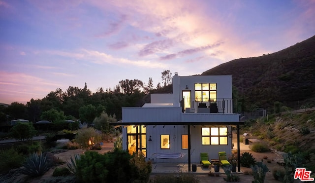 back house at dusk with a patio area, a mountain view, and a balcony