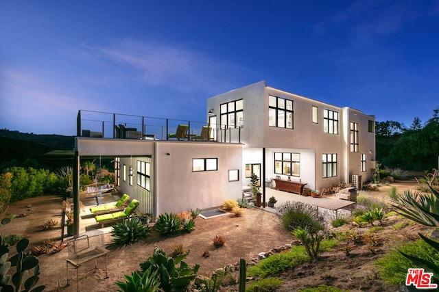 back house at dusk featuring a balcony and a patio area