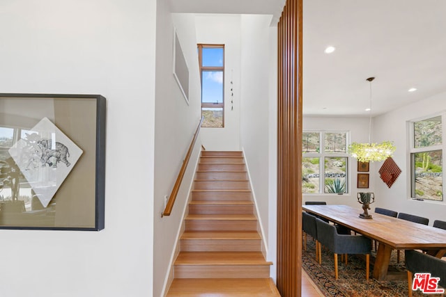 stairway featuring hardwood / wood-style floors, a notable chandelier, and a wealth of natural light