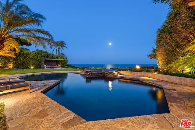 pool at dusk with a patio area, an in ground hot tub, and a water view