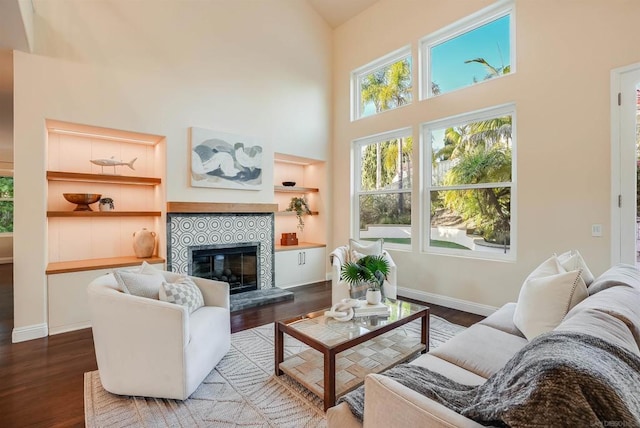 living room with a tile fireplace, built in shelves, a towering ceiling, and hardwood / wood-style flooring