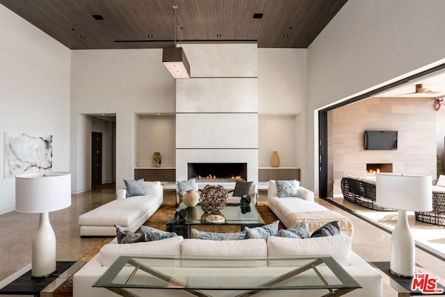 living room with a large fireplace, a towering ceiling, and wood ceiling