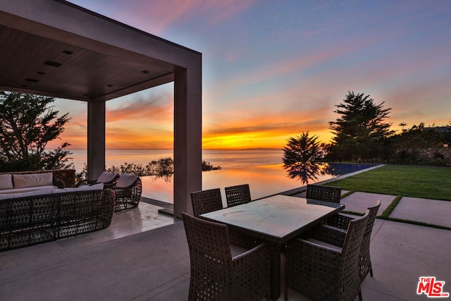 patio terrace at dusk featuring an outdoor living space, a water view, and a yard